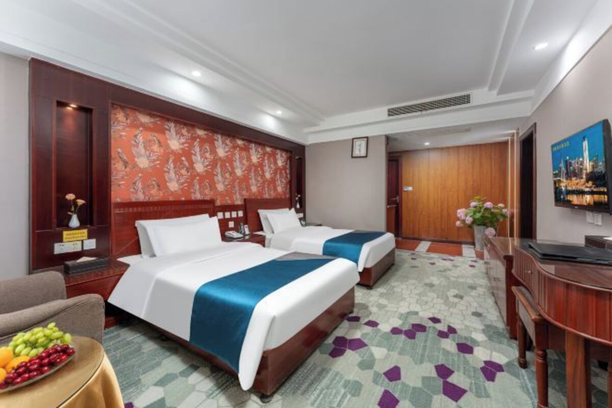 Una habitación de hotel con dos camas, un escritorio, una silla y una mesita con fruta.