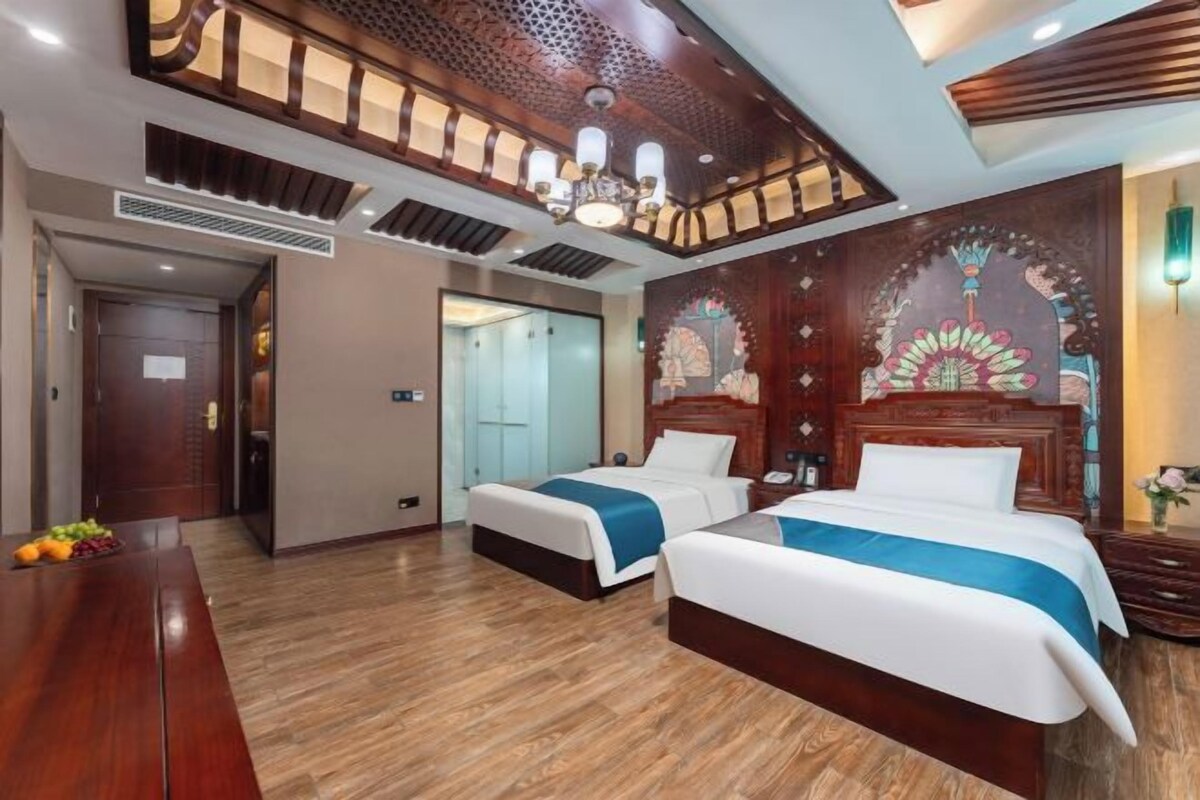 A hotel room with two beds, a wooden floor, a chandelier, and decorative wall art.