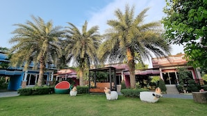 A garden with palm trees, a watermelon sculpture, and a gazebo. - Baan Suan  Meetang Resort (Chanthaburi)