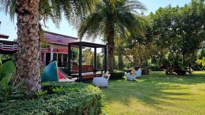 A garden with a gazebo, palm trees, and a building with a red roof. - Baan Suan  Meetang Resort (Chanthaburi)