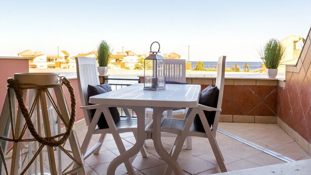 Een balkon met een witte tafel en stoelen, een lantaarn en potplanten.