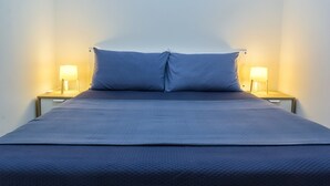 Een bed met een blauwe matras en kussens, met aan weerszijden nachtkastjes met lampen.