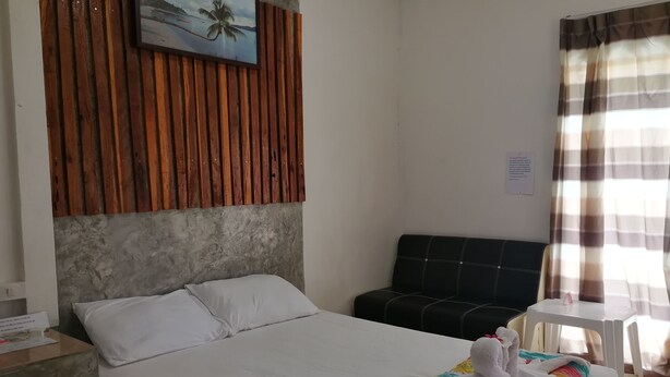 Habitación de hotel con una cama, cabecera con diseño de panel de madera, sofá negro, una mesita blanca y una ventana con cortinas.