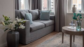 A modern living room with a grey sofa, a round wooden coffee table, and a vase with flowers.