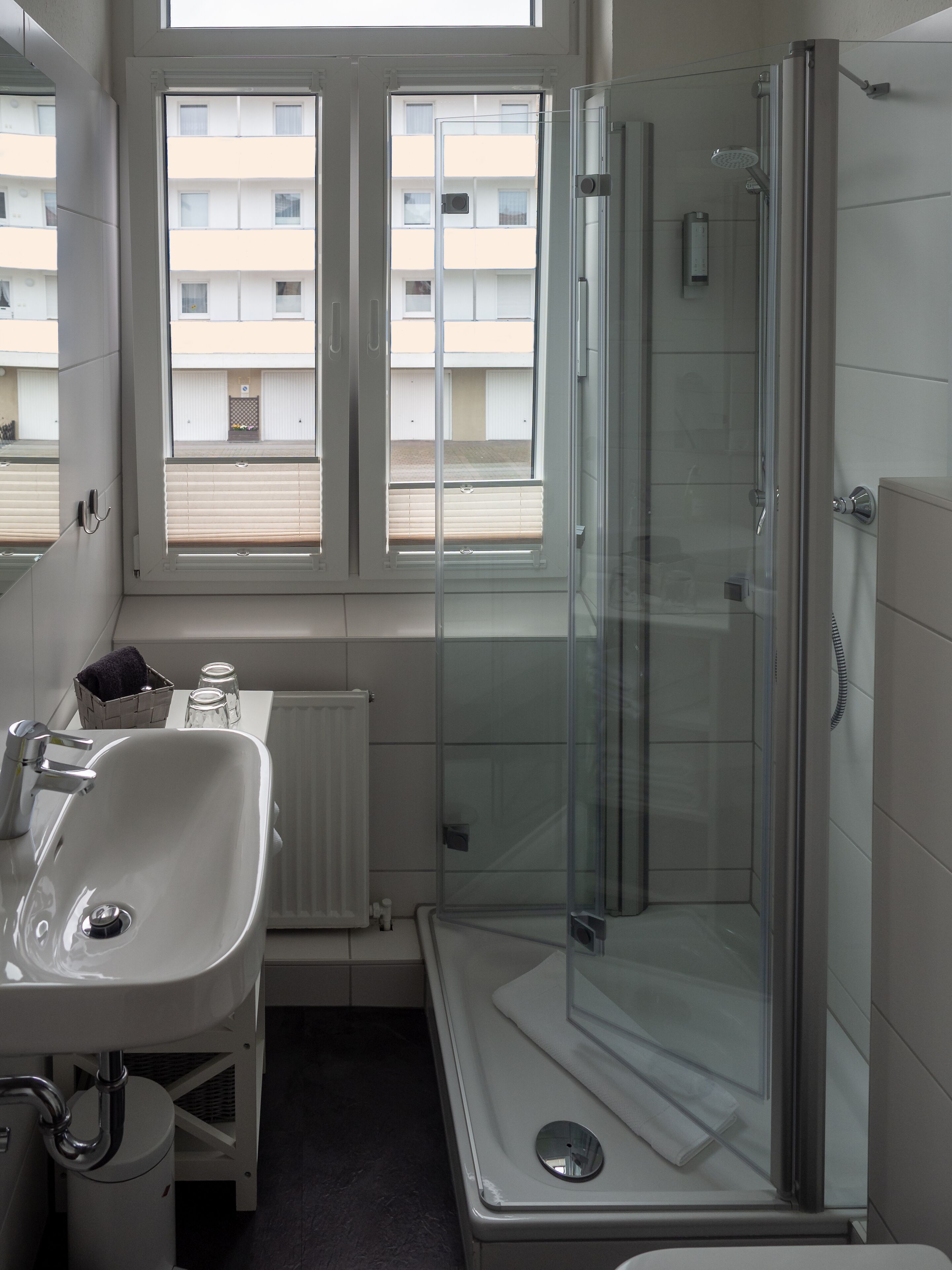Un bany modern amb un espai de banyera de vidre, un lavabo blanc i una finestra amb persianes.
