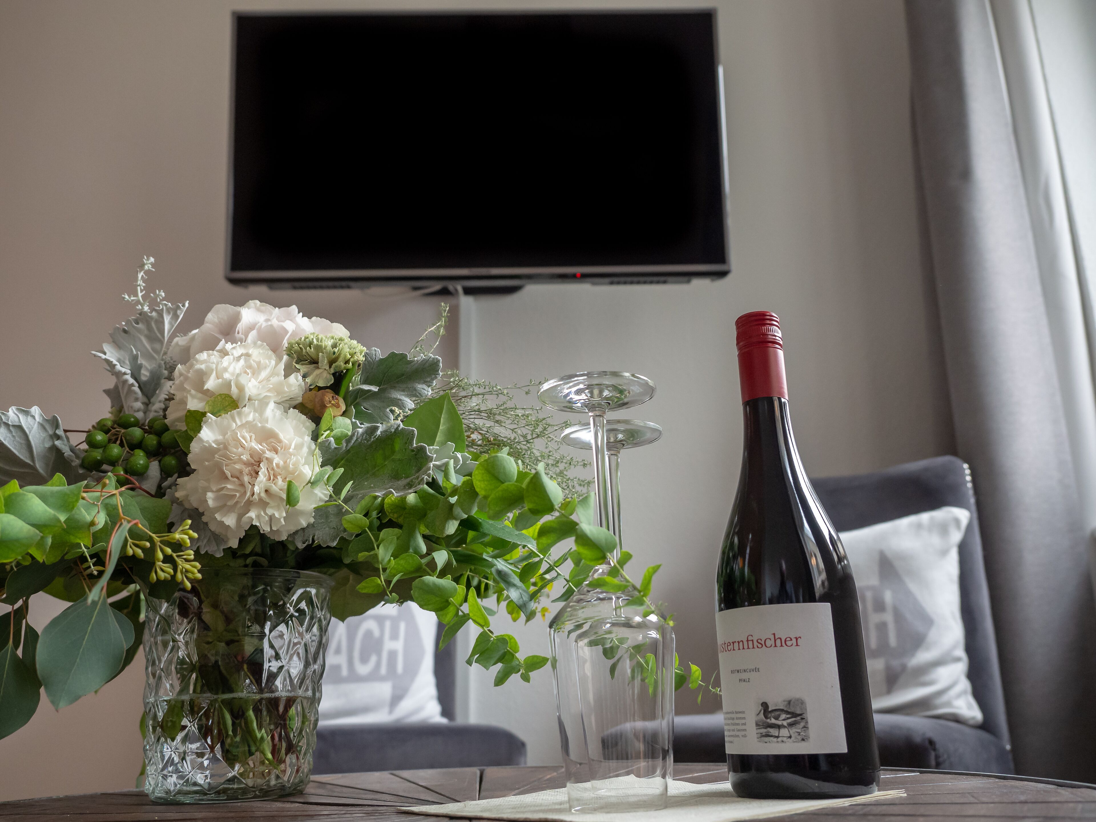 A table with a wine bottle, a glass, and a vase of flowers.