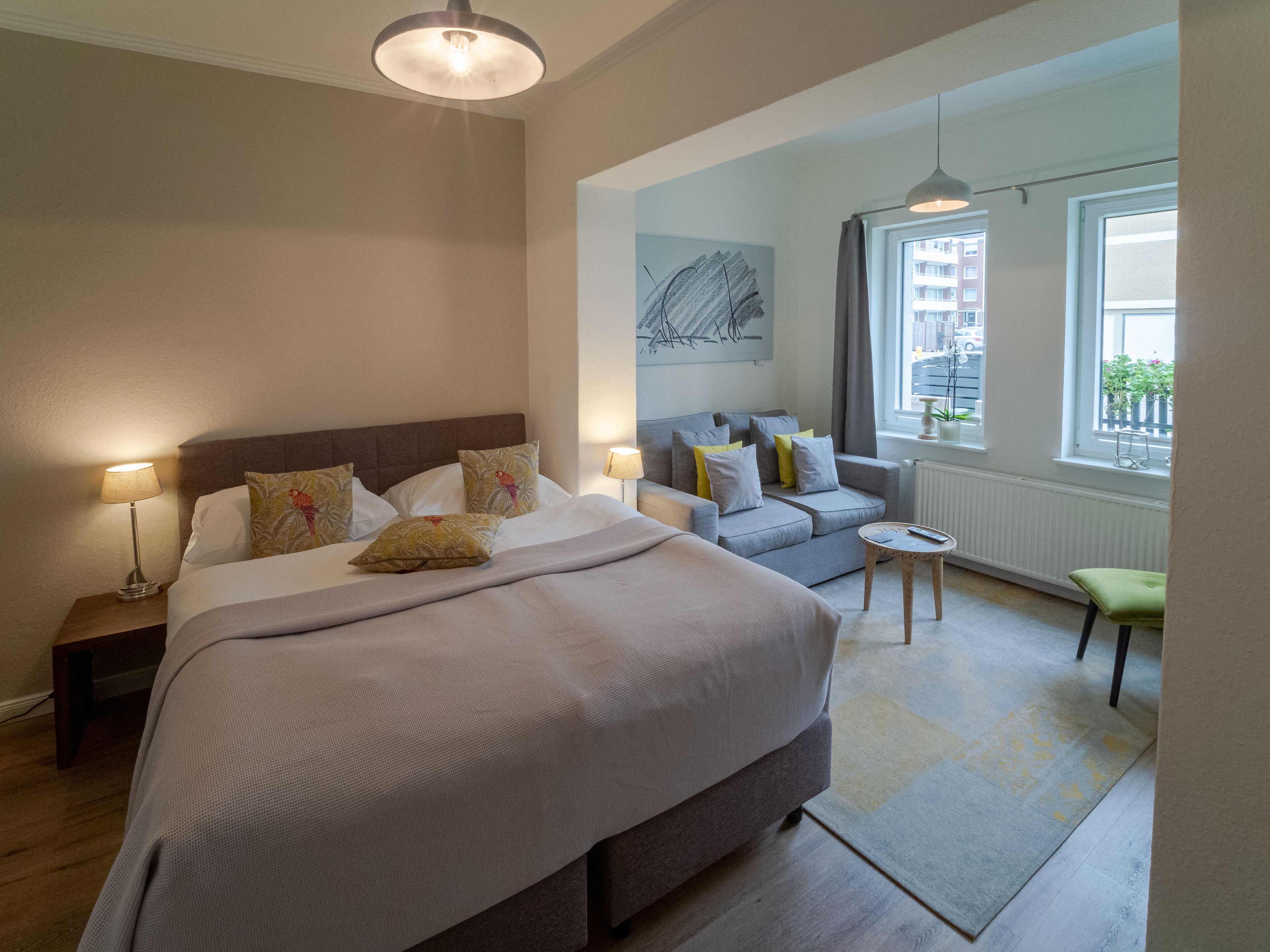 Ein modernes Hotelzimmer mit einem großen Bett, einer Couch, einem kleinen Tisch und Blick auf die Stadt durch das Fenster.