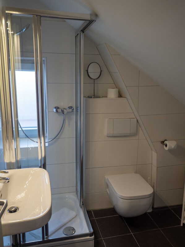 Un baño moderno con cabina de ducha de vidrio, un lavabo blanco, un inodoro y un espejo pequeño.