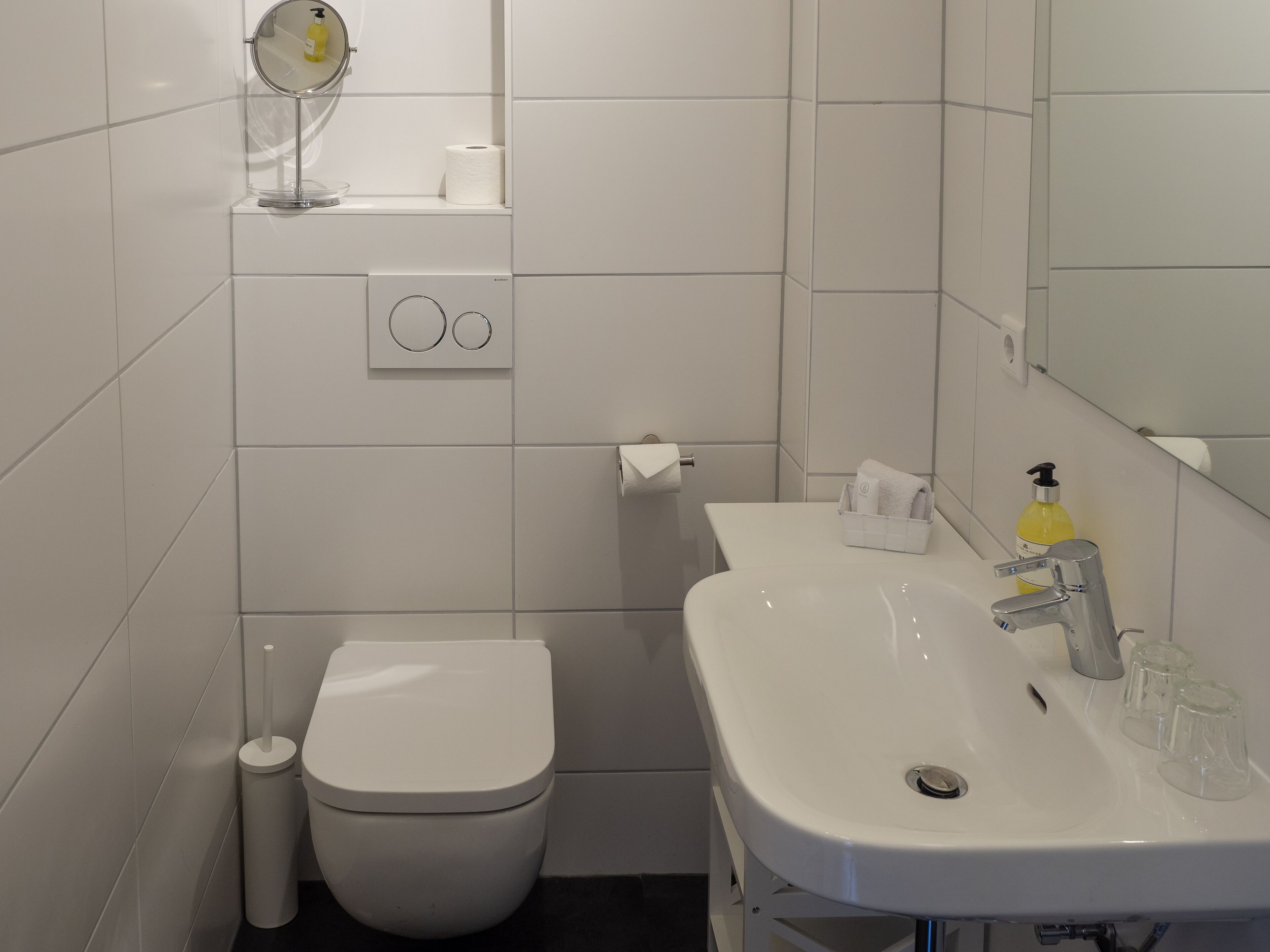 A bathroom with a toilet, sink, mirror, and a soap dispenser.