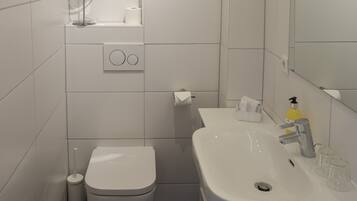 A bathroom with a toilet, sink, mirror, and a soap dispenser.