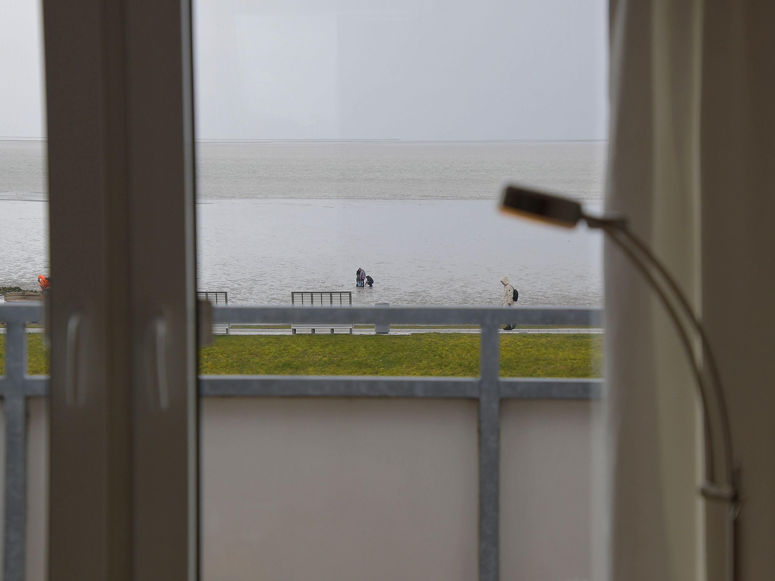 Blick aus einem Fenster auf einen Strand, mit Geländer und einer Lampe.