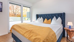 A bedroom with a large bed, a window with a view of trees, and a nightstand with a lamp. - Apartment 4 Deluxe Apartment 51 sqm, 1-4 persons, balcony and wonderful mountain view (Bayerisch Gmain)