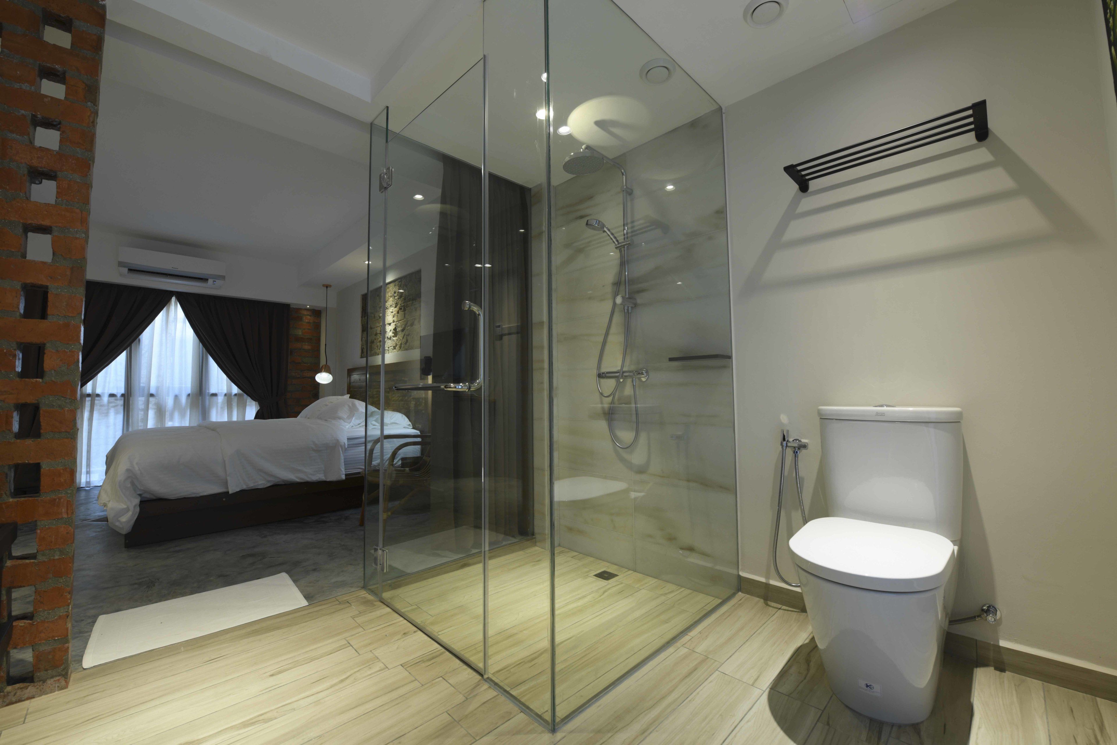 A modern bathroom with a glass-enclosed shower, a toilet, and a bed in the adjacent room.