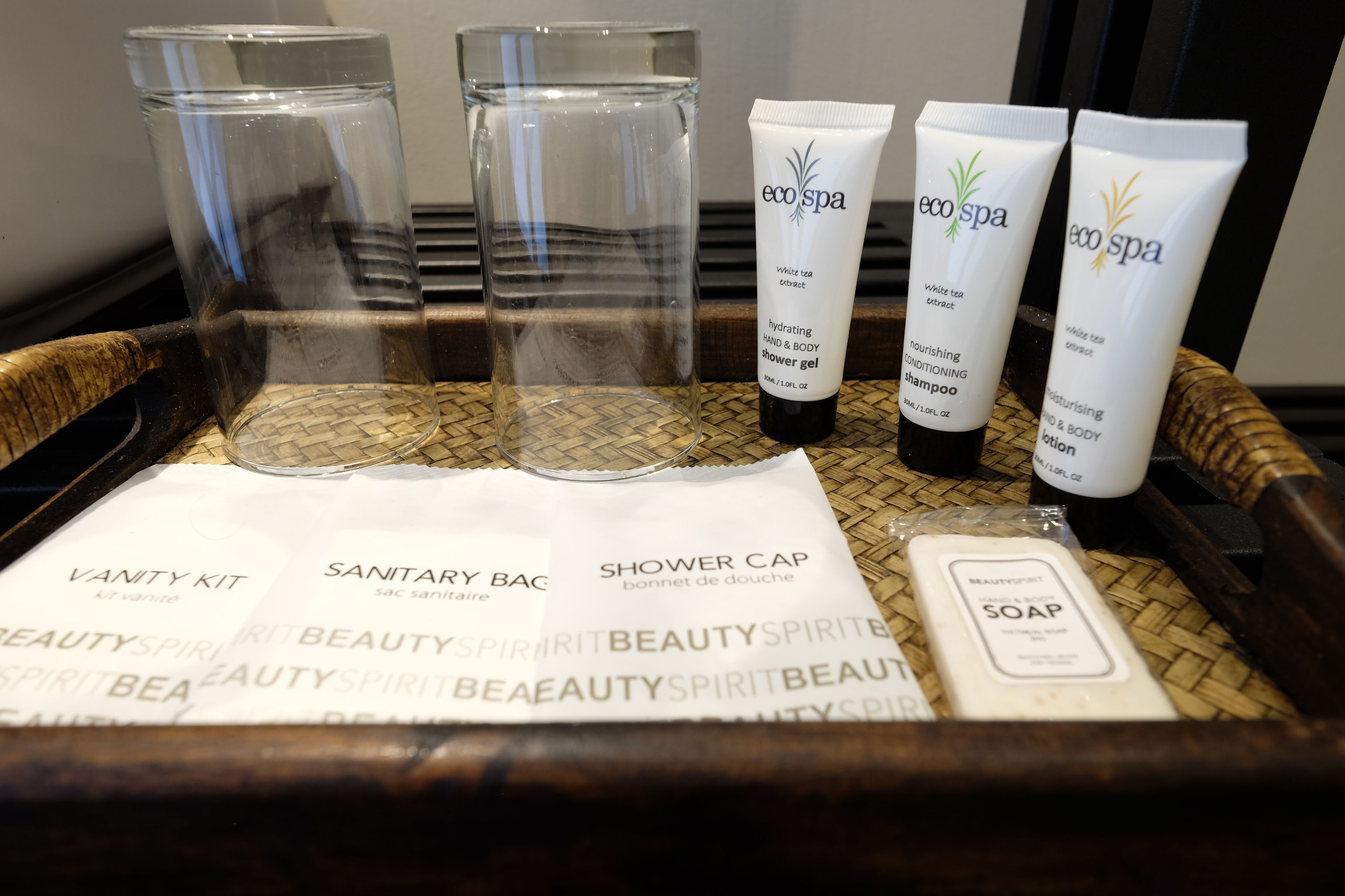 A tray with a vanity kit, sanitary bag, shower cap, and toiletries including shampoo, conditioner, and soap.