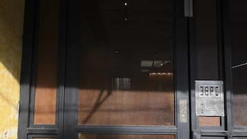 A building entrance with a large glass door, a sign with '38PC' on it, and a tiled ground.