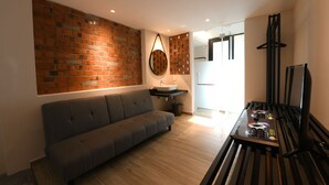 A modern living room with a grey sofa, a brick accent wall, a round mirror, a small table with a sink, and a black TV stand.