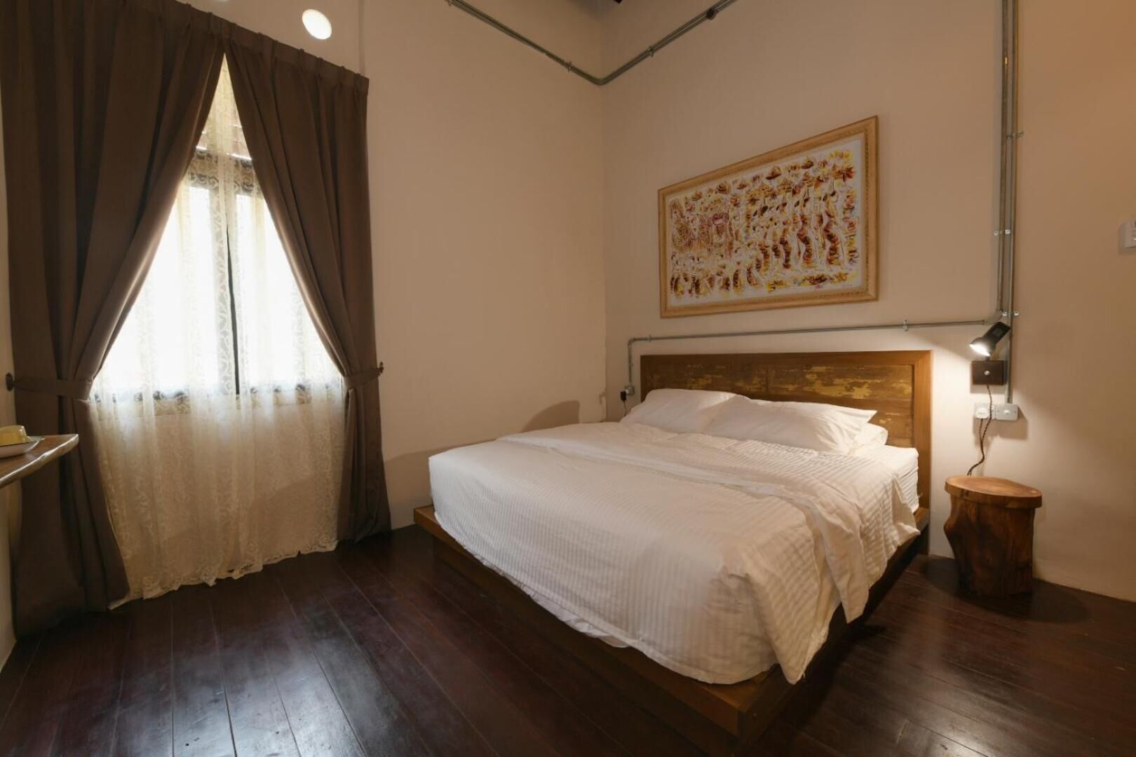 Un dormitorio con cama de madera, mesita de noche, lámpara, ventana con cortinas y un cuadro en la pared.