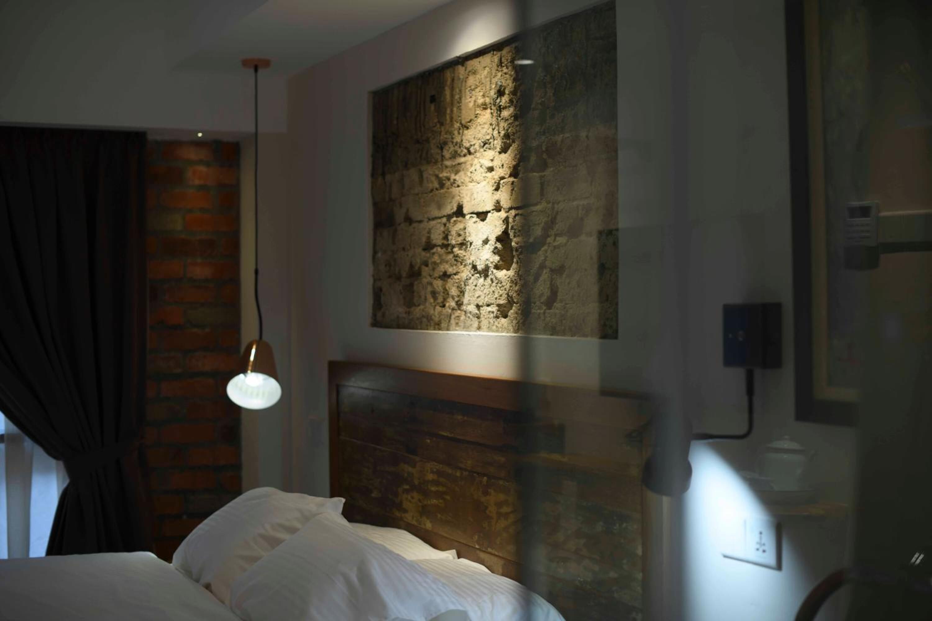 Ein Schlafzimmer mit Backsteinwand, Holz-Kopfteil, einer Pendelleuchte und einem Fenster mit Vorhängen.