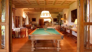 Une salle de billard équipée d’une table de billard, dotée d’un plancher en bois et d’un plafond haut orné de moulures décoratives.
