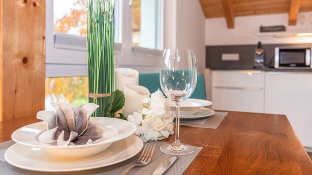 Una mesa de comedor dispuesta con platos, una copa de vino y un florero con flores.