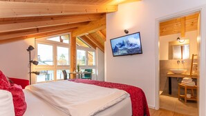 Un dormitorio con cama, televisor montado en la pared y baño visible a través de una puerta abierta.