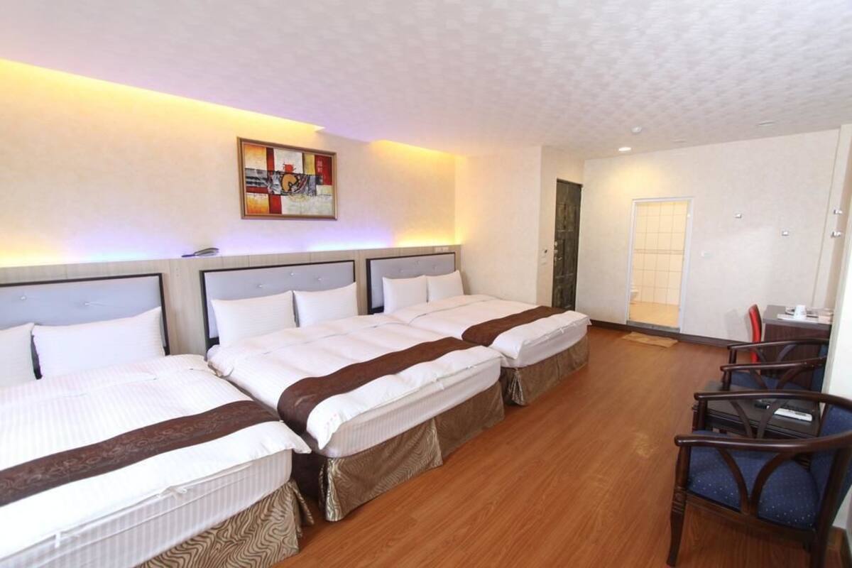A hotel room with three beds, a desk, and a chair.