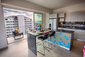 A modern kitchen with a bar area, large windows, and a balcony with seating.