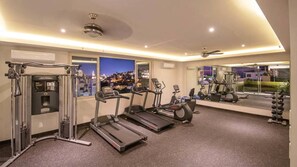 Et fitnesscenter med løbebånd, styrkemaskine og et spejl der viser bybilledet.