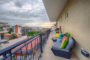 En balkon med sofa, puder, gelænder og udsigt over bybilledet.