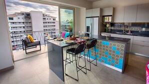 Una cocina moderna con una isla grande, taburetes de bar y vistas a un paisaje urbano a través de amplios ventanales.