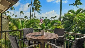 An outdoor patio with wicker furniture, a round wooden table, and a potted orchid. - Kahala at Poipu Kai #121 By Parrish Kauai - walk to Poipu Beach & great for hone (Koloa)