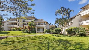 A residential building with a two-story structure, a balcony, and a well-maintained lawn with various plants.