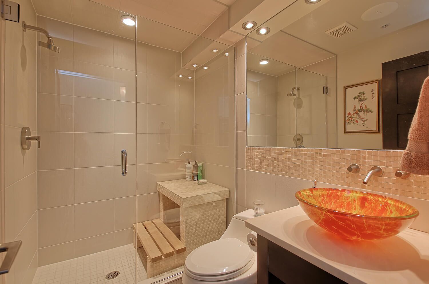 A modern bathroom with a glass-enclosed shower, a white toilet, and a large glass bowl sink.