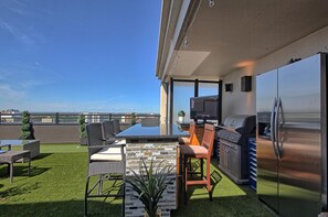 Un patio en la azotea con comedor, una parrilla y un refrigerador grande.