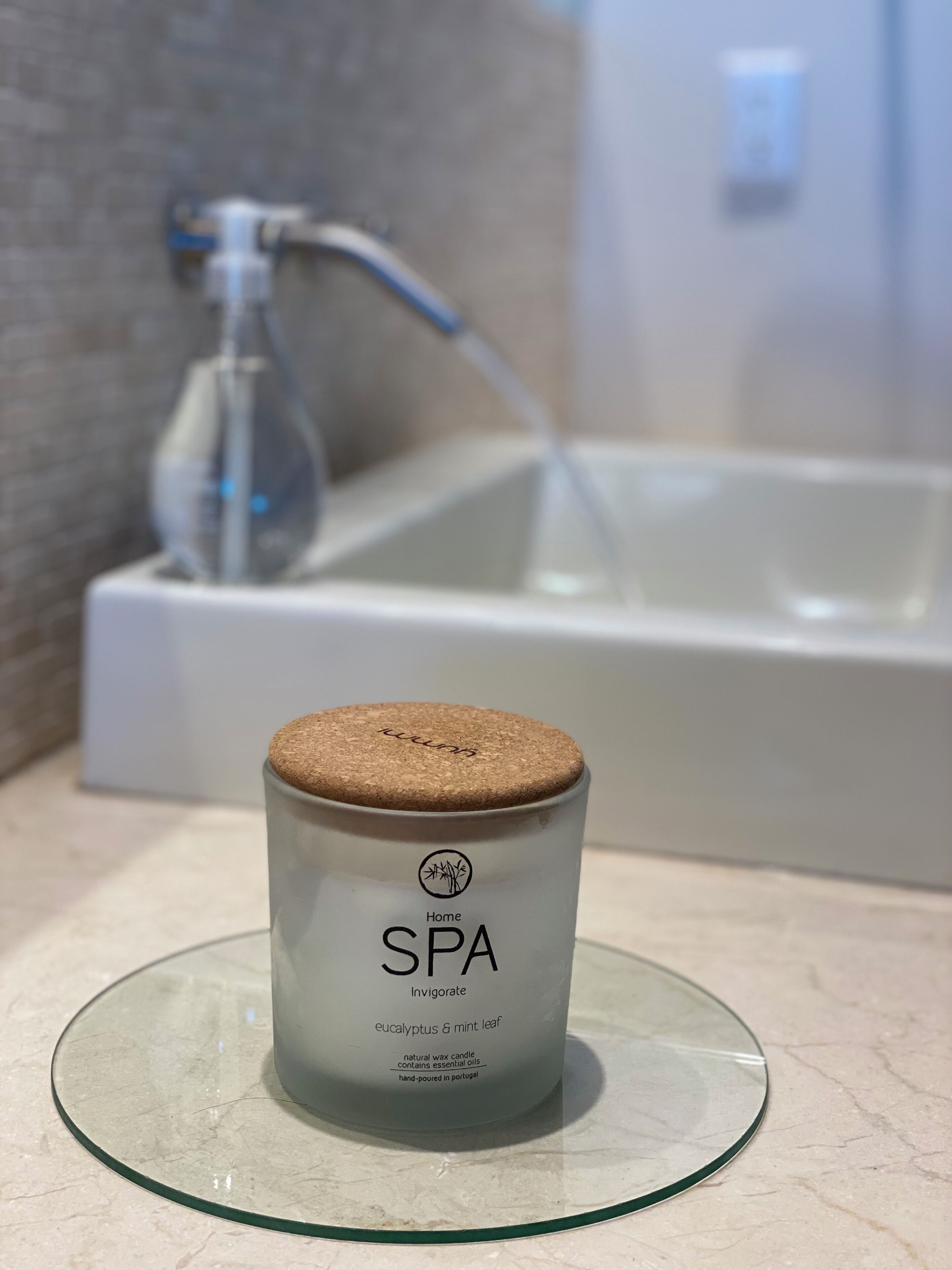 Une salle de bain avec un porte-bougie en verre posé sur un comptoir en marbre, une baignoire blanche et un robinet visible au fond.