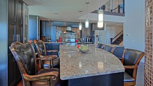 A modern kitchen with a central island, dark cabinetry, and a dining area with leather chairs. - Luxury Penthouse Oasis, Rooftop Patio, River View, Downtown (Edmonton)