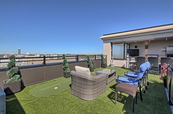 A rooftop terrace with wicker furniture, a flat-screen TV, and a view of the cityscape.