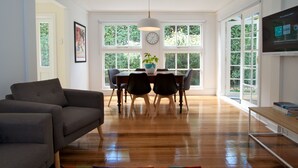 Un salón amplio con un sofá gris oscuro, una mesa de comedor de madera con sillas y un ventanal con vistas a la vegetación.