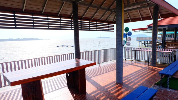 A wooden deck with a table and benches, overlooking a body of water with boats and a distant island. - Khuntim Homestay Koh Rat (Koh Samui)