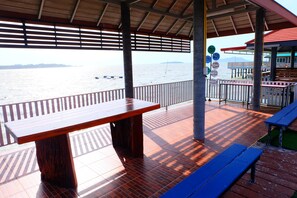 A wooden deck with a table and benches, overlooking a body of water with boats and a distant island. - Khuntim Homestay Koh Rat (Koh Samui)