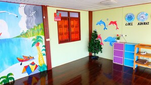 A room with a wooden floor, a mural with sea and sky, a Christmas tree, a desk with a computer, and two clocks on the wall. - Khuntim Homestay Koh Rat (Koh Samui)