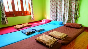 A room with two beds, each with a different colored bedspread and pillows. There are curtains on the windows, and the room has a wooden floor. - Khuntim Homestay Koh Rat (Koh Samui)