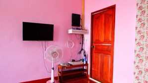 A pink-walled room with a wooden door, a mounted TV, a pink fan, and a shelf with electronic devices. - Khuntim Homestay Koh Rat (Koh Samui)