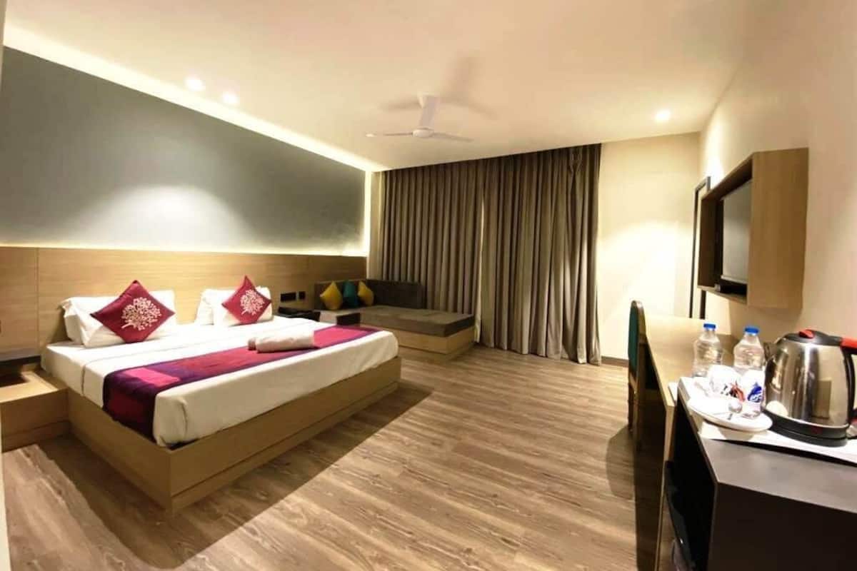 A hotel room with a bed, a desk, a chair, a flat-screen TV, a ceiling fan, and a window with curtains.
