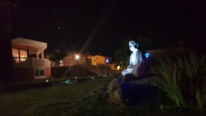 A statue of a seated figure in a garden at night with illuminated signs and a building in the background. - Poreč Sunshine (Porec)
