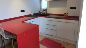 A compact kitchen with a red countertop, white cabinets, a sink, and a small window. - B&B Le Peschiere (Montefiorino)