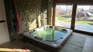 A hot tub in a room with stone walls, a wooden ceiling, and a view of a parking area through a glass door. - B&B Le Peschiere (Montefiorino)