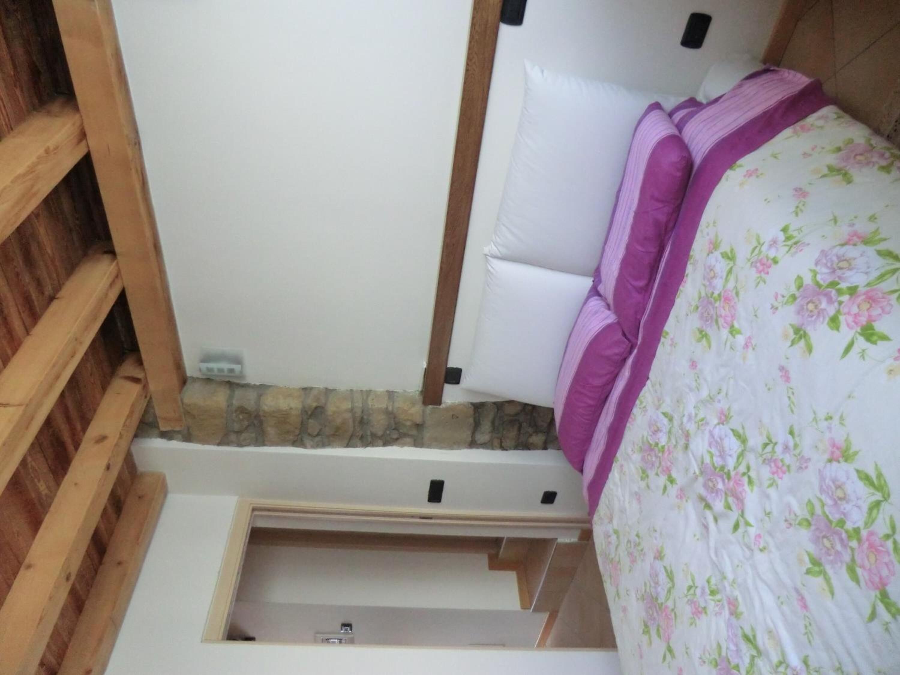 Un dormitorio con una cama, una escalera de madera, una pared blanca y una pared de piedra.