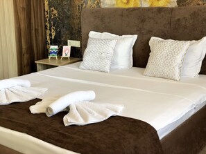 A neatly made bed with white linens and geometric patterned pillows, a brown headboard, and a small bedside table with a lamp and a framed picture. - Flamingo Plovdiv (Plovdiv)