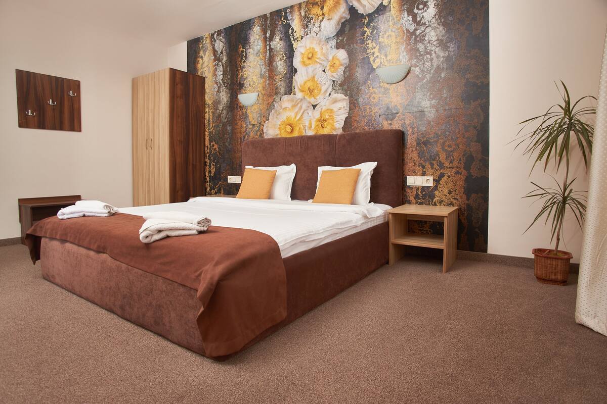A bedroom with a large bed, wooden wardrobe, and a decorative wall mural.